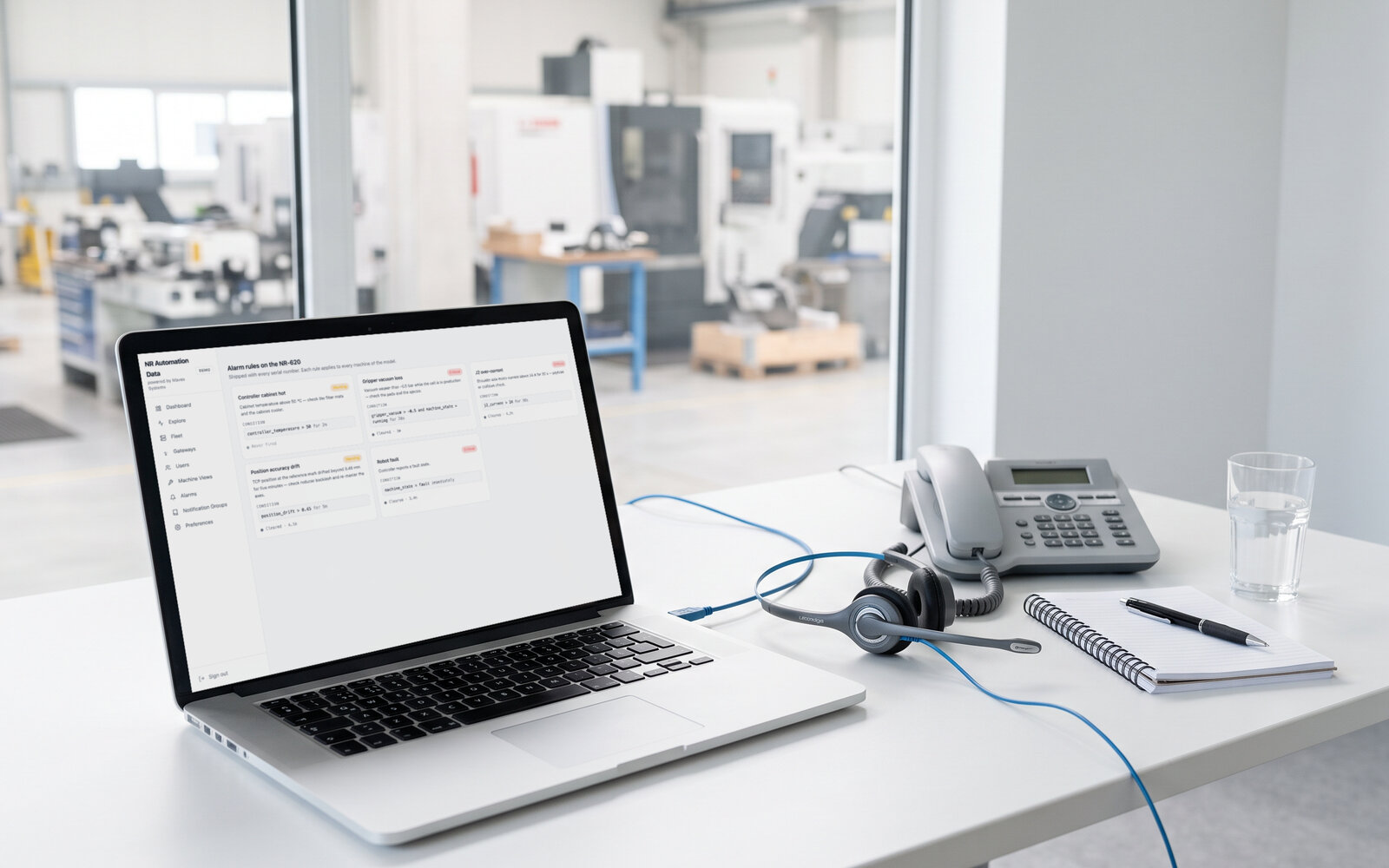 A machine builder's service desk: a laptop showing the alarm rules of a machine model under the customer's own brand, a headset and a desk phone beside it, the hall far behind the window. Demo data, illustrative photo.